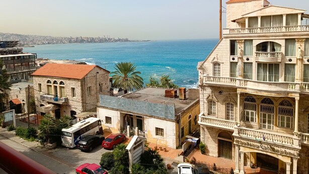 A coastal cityscape with historic buildings, a view of the sea, and parked vehicles. - EdwardVHotel (Jounieh)