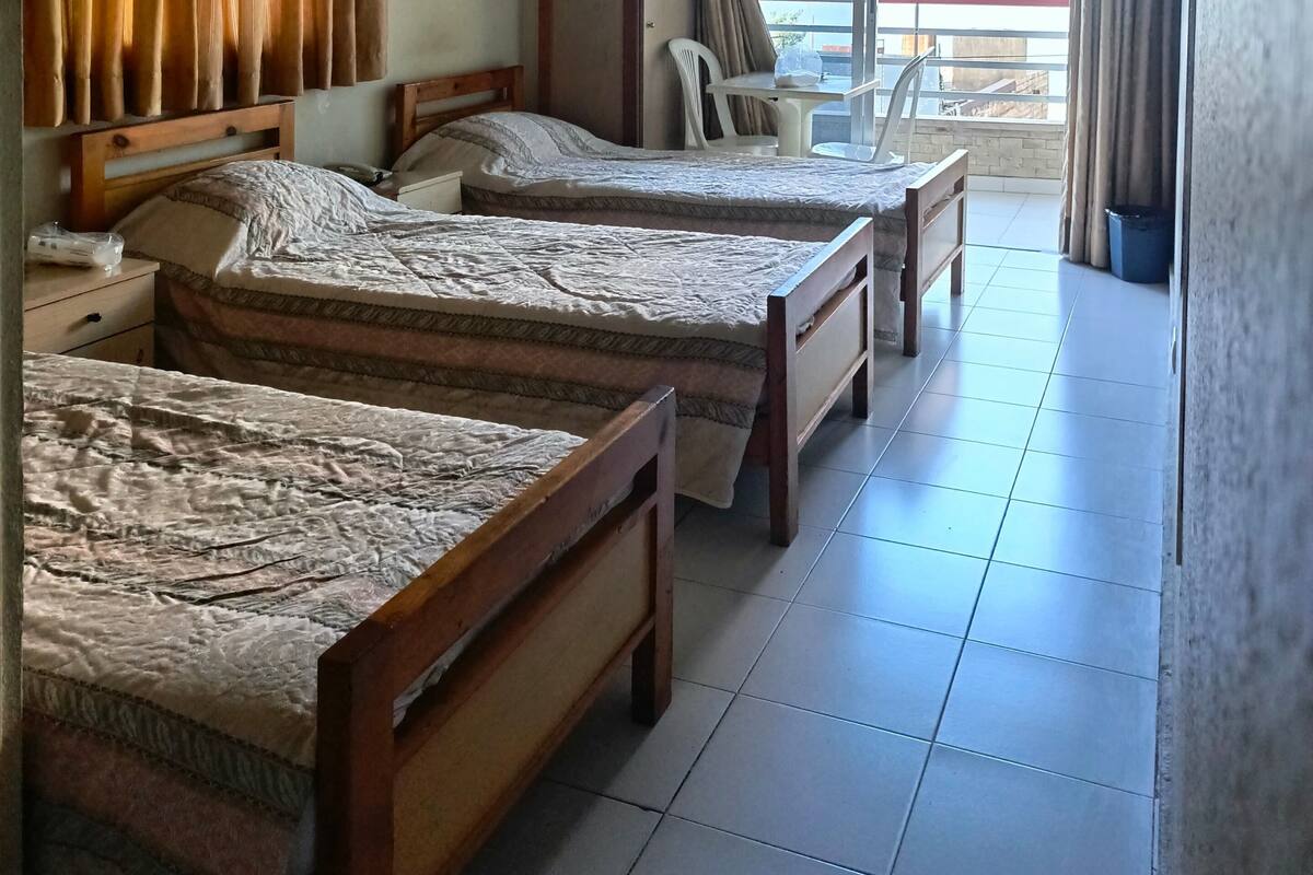 A hotel room with two wooden beds, a small table, a chair, and a balcony with a view.