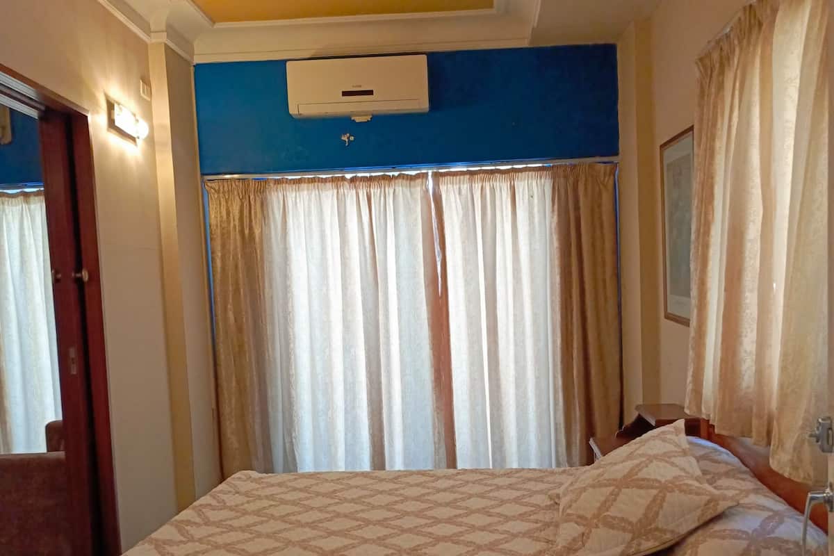 A bedroom with a large bed, a ceiling air conditioner, and curtains.