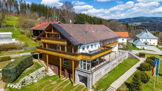 A two-story wooden house with a balcony, surrounded by a well-maintained garden and a clear view of the surrounding landscape. - Stunning private villa for 36 guests with WIFI, TV and terrace (Bayerisch Eisenstein)