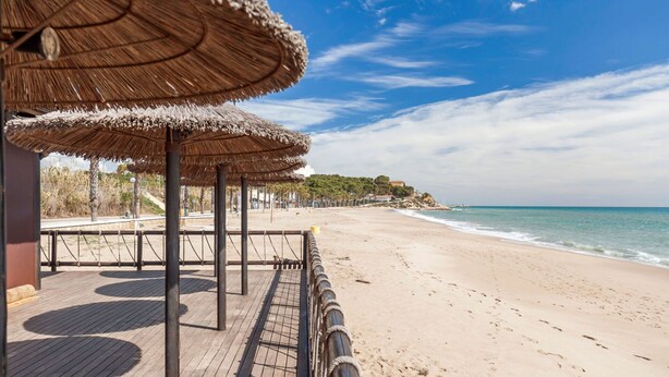 Une plage avec une terrasse en bois et des parasols en chaume, donnant sur la mer.