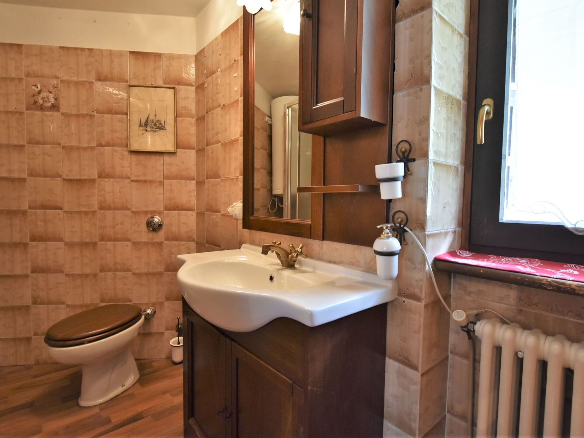 A bathroom with a wooden toilet, a white sink with a gold faucet, a mirror above the sink, and a radiator on the right.