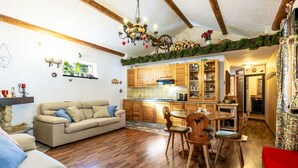 A cozy living room with a sofa, a dining table with chairs, wooden flooring, and a kitchen with wooden cabinets and a chandelier. - Lovely apartment for 4 people with WIFI, TV, terrace and pets allowed (Isola)