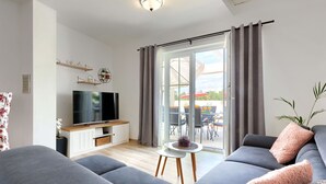Ett modernt vardagsrum med en grå soffa, en platt-TV och en skjutdörr i glas som leder ut till en uteplats.