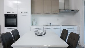 A modern kitchen with white cabinets, a black oven, a stainless steel range hood, a white countertop, and a dining table with four chairs. - Beautiful apartment for 5 people with A/C, WIFI, TV, balcony and pets allowed (Solin)