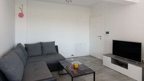 A modern living room with a grey sectional sofa, a glass coffee table with a drink, a flat-screen TV on a white cabinet, and a door with a lock. - Beautiful apartment for 5 people with A/C, WIFI, TV, balcony and pets allowed (Solin)