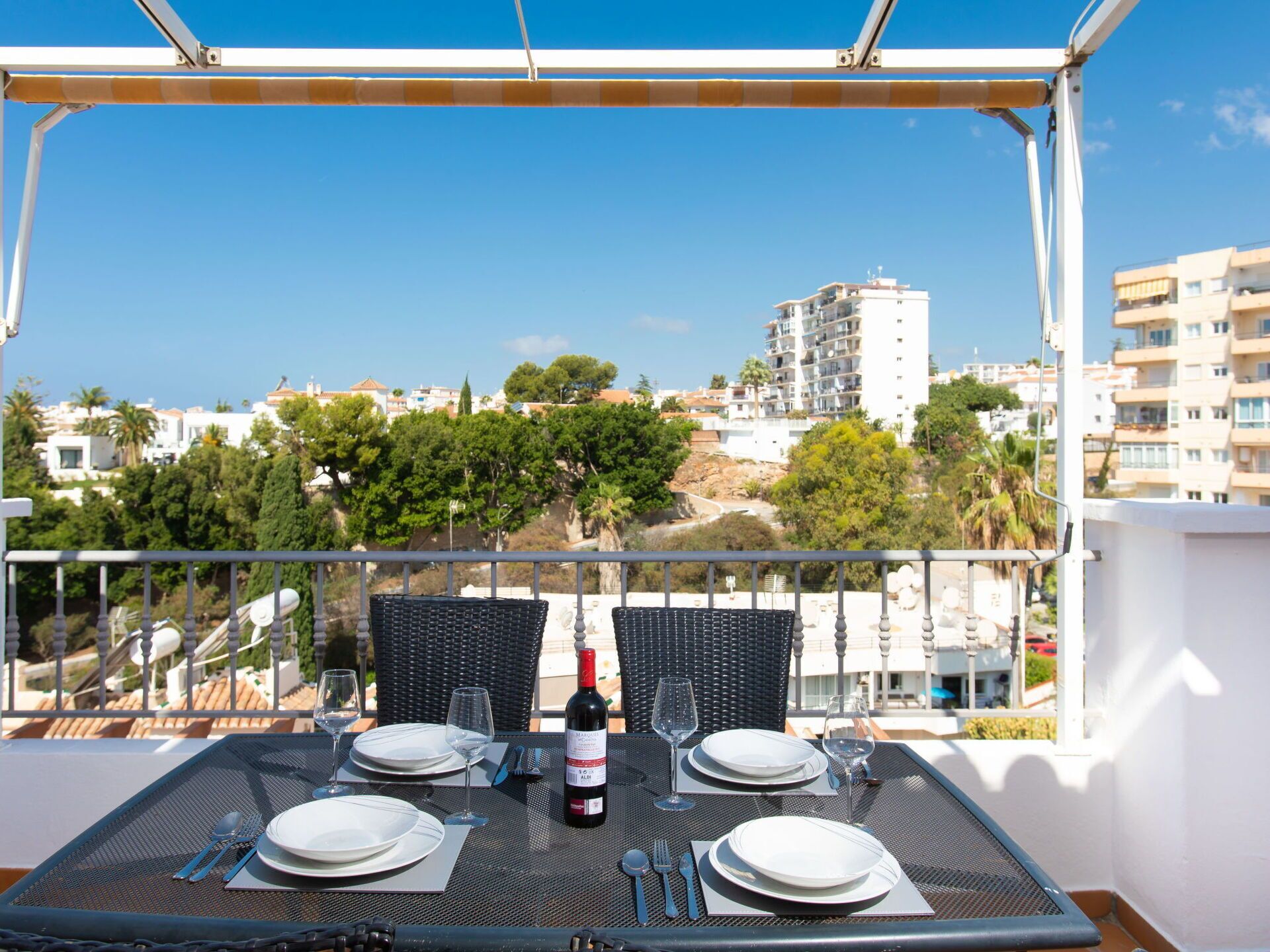 Uma varanda com uma mesa posta para dois, com vista para um horizonte urbano com edifícios e árvores.