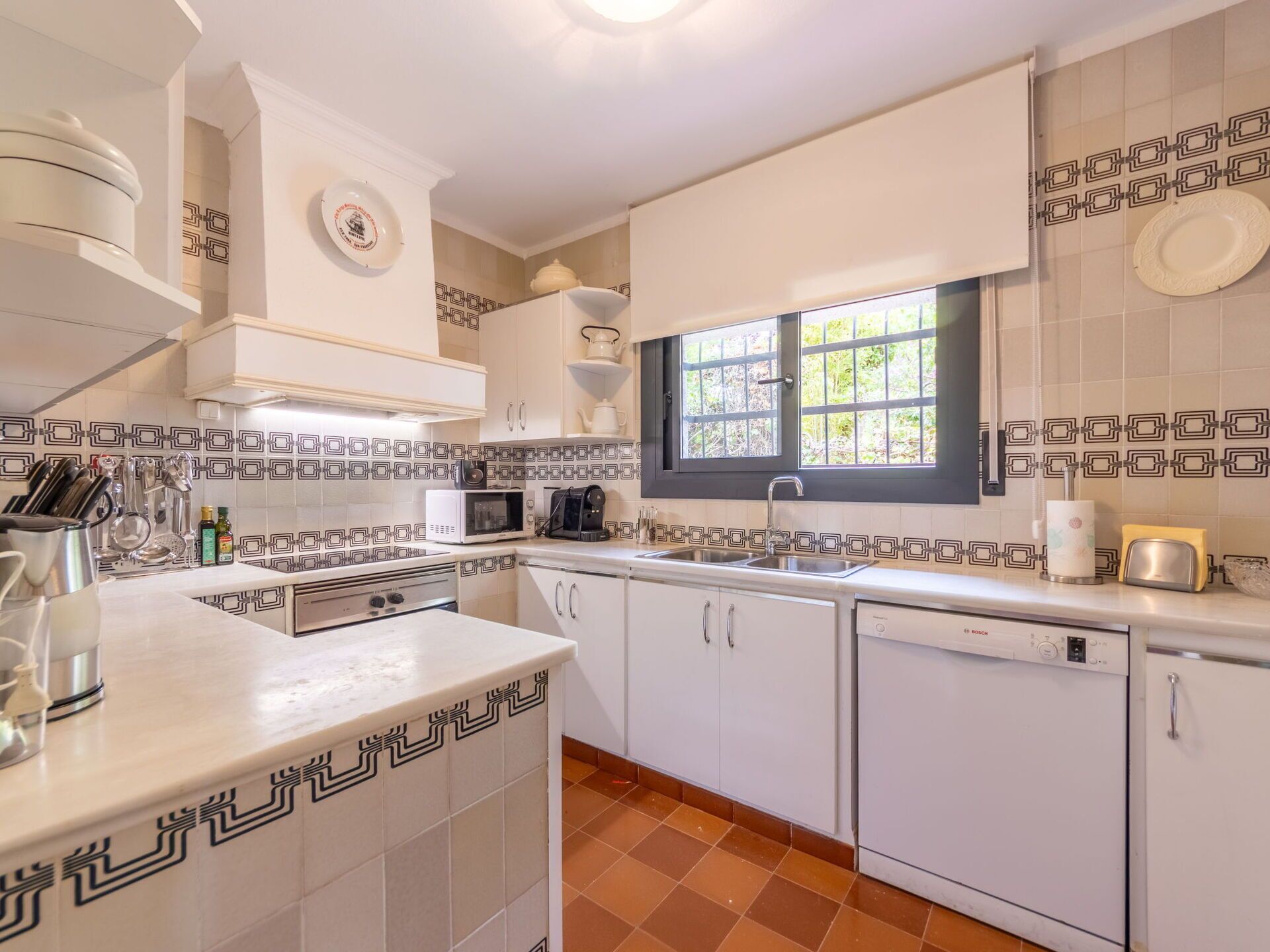 A modern kitchen with white cabinets, a microwave, a coffee maker, and a window with a view of greenery.
