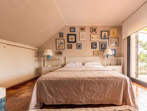 A bedroom with a large bed, two bedside tables with lamps, a wall decorated with framed pictures, and a window providing a view of greenery. - Beautiful private villa for 8 guests with WIFI, A/C, private pool, TV, terrace and pets allowed (El Vendrell)