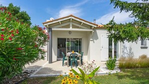 Une maison dotée d’un patio couvert, d’un coin repas avec des chaises et d’un jardin fleuri.
