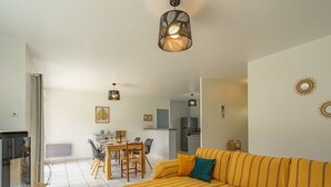 Un salon moderne avec un canapé, une table à manger et des chaises. On aperçoit un coin cuisine au fond de la pièce.