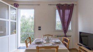 Un comedor con una mesa preparada para cuatro personas, un televisor y una ventana con cortinas moradas.