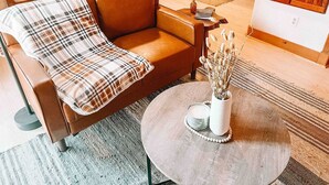 A modern living room with a brown leather sofa, a round coffee table, and a dining area in the background. - Private Forest Retreat | Ruidoso Couples Escape (Ruidoso)