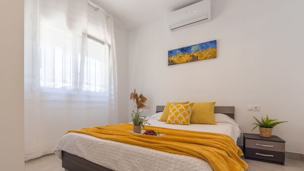A bedroom with a bed, a window with curtains, an air conditioner, a painting, a bedside table with a plant, and a bedside lamp. - Wonderful private villa for 7 guests with WIFI, A/C, TV and pets allowed (Amposta)