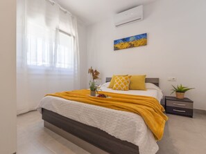 A bedroom with a bed, a window with curtains, an air conditioner, a painting, a bedside table with a plant, and a bedside lamp. - Stunning private villa for 7 guests with WIFI, A/C, TV and pets allowed (Amposta)