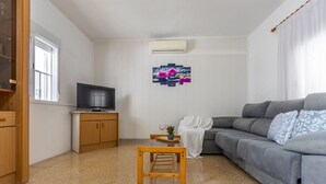 A living room with a grey sofa, a wooden coffee table, a television on a wooden cabinet, and a window with blinds. - Wonderful private villa for 7 guests with WIFI, A/C, TV and pets allowed (Amposta)