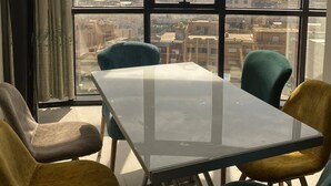Una habitación con un amplio ventanal que ofrece vistas a la ciudad, una mesa de vidrio y cuatro sillas.