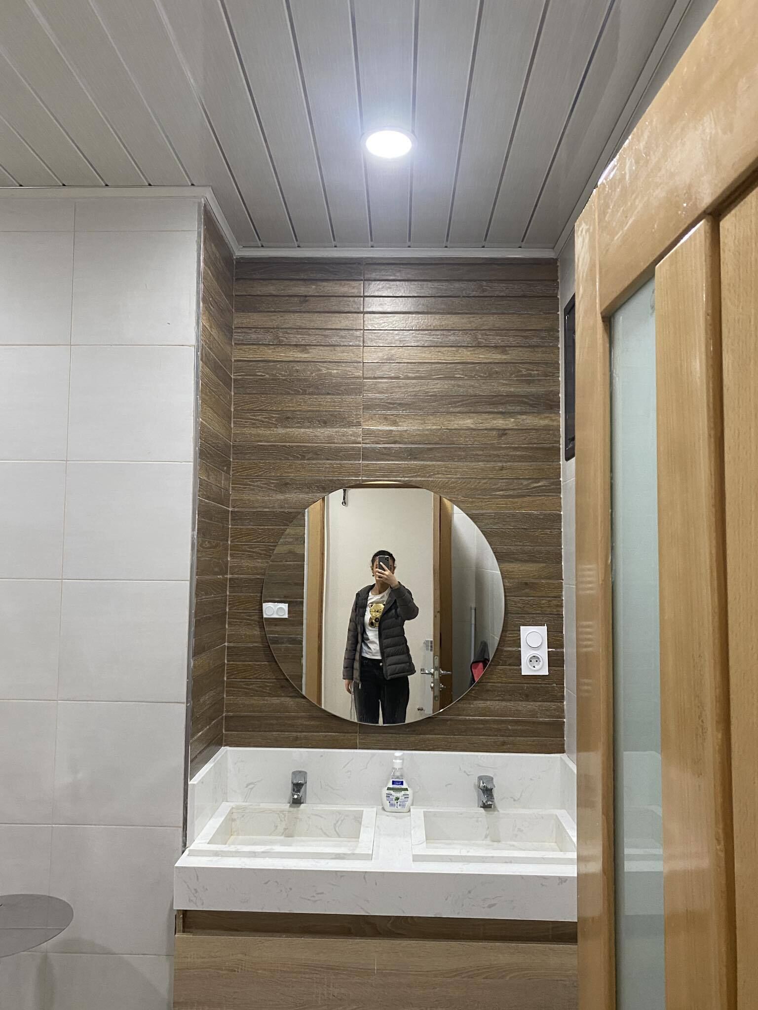 A bathroom with a wooden panel wall, a round mirror, and two sinks.