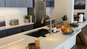 Una cucina moderna con isola centrale, elettrodomestici in acciaio inossidabile e una zona relax con divano in pelle marrone.