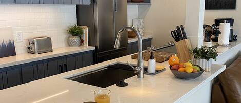 A modern kitchen with a central island, stainless steel appliances, and a seating area with a brown leather couch.