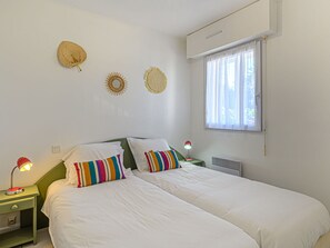 Two single beds with white linens and colorful pillows, set against a white wall, offer a simple and clean retreat.