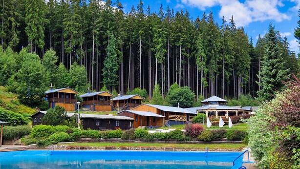 Een resort met meerdere houten bungalows, een zwembad en een bebost achtergrond.