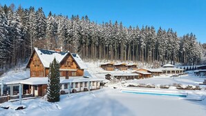 En snötäckt stuga med flera trähytter, en swimmingpool och en skog som bakgrund.