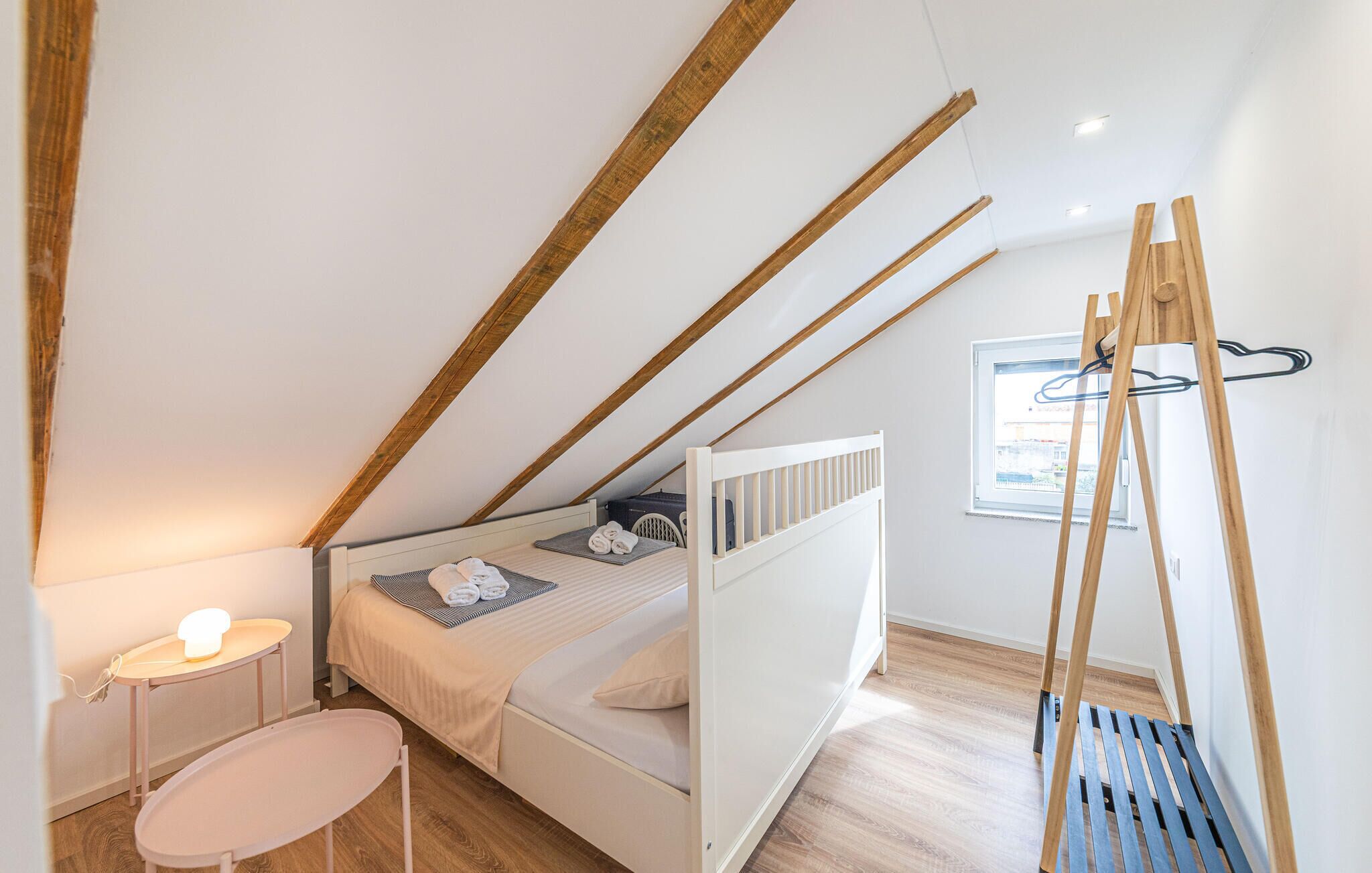 Un dormitorio con techo inclinado, una cama, una mesita de noche, una lámpara y una ventana.