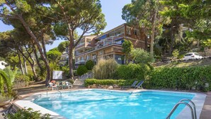 A swimming pool surrounded by trees and a building with balconies. - Cosy apartment for 4 people with A/C, pool, WIFI, TV and terrace (Tossa De Mar)