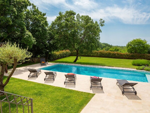 A swimming pool with four lounge chairs and a small table, surrounded by well-maintained grass and trees.