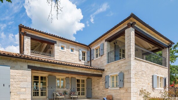 A two-story stone house with a balcony and a covered patio area.