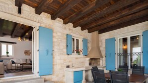 A stone-walled kitchen with blue cabinets and a chimney, a dining area with chairs, and a staircase leading to an upper level. - Wonderful private villa with private pool, WIFI, A/C, TV, terrace, pets allowed and panoramic view (Pazin)