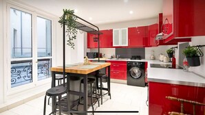 A modern kitchen with red cabinets, a wooden dining table, and a built-in washing machine.