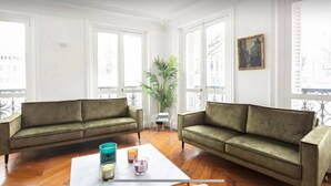 A living room with two green sofas, a coffee table with candles, and a large plant.
