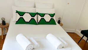 A neatly made bed with white linens and two green and white pillows. There are two rolled white towels on the bed.