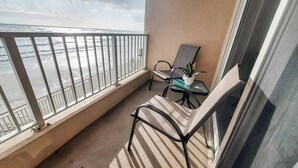 A balcony with a view of the sea, a chair, a small table with a plant, and a window.