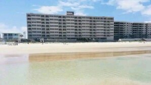 A multi-story hotel with a flat roof and a uniform facade, located adjacent to a sandy beach.