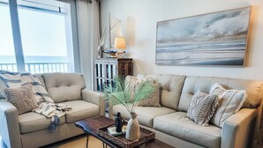 A living room with a beige sofa, a wooden coffee table, and a large window with curtains.