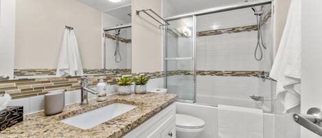 Une salle de bain moderne avec un comptoir en granit, une douche en verre et des toilettes blanches.