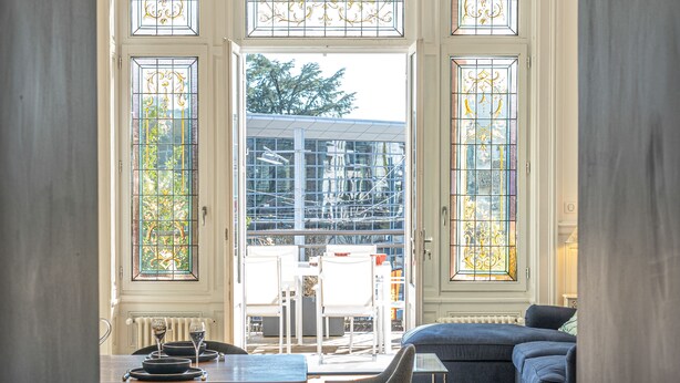 Una habitación amplia con una mesa de comedor, sillas y un sofá. Cuenta con ventanas grandes y vidrios decorativos.
