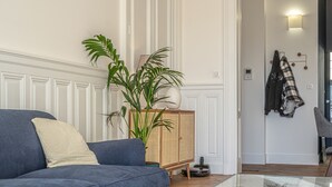 Una sala de estar con un sofá azul, una pared blanca, una planta y una puerta con interruptor de luz y termostato.