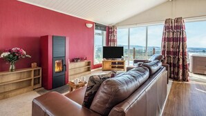 Un salón amplio con una pared roja, una chimenea, un sofá de cuero y un gran ventanal con vistas al exterior.