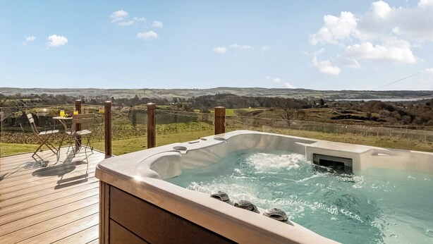 Un jacuzzi en una terraza de madera con vistas panorámicas de colinas ondulantes y cielo despejado.