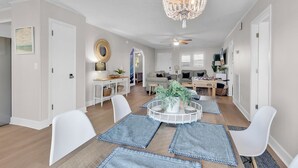 A modern living room with a dining area, white walls, and a chandelier. - Waterfront Home: 4 min walk to beach, Pool & Mini-Golf (North  Myrtle Beach)