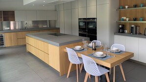 A modern kitchen with a central island, built-in appliances, and a dining area with chairs and table set for four. - Beautiful Divonne Home in the Heart of the town and totally Private! (Divonne-les-Bains)