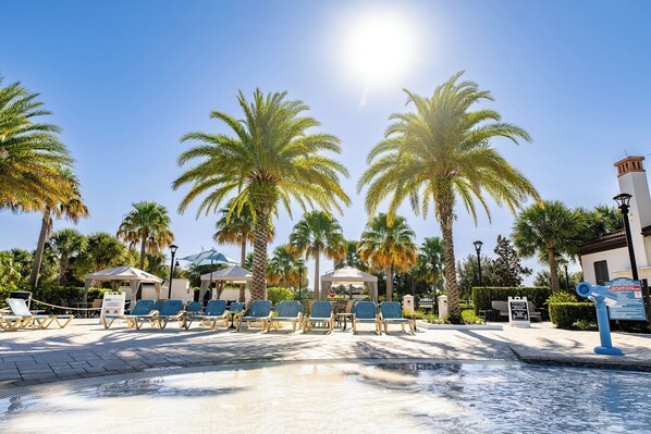 A poolside area with lounge chairs, palm trees, and a clear sky.
