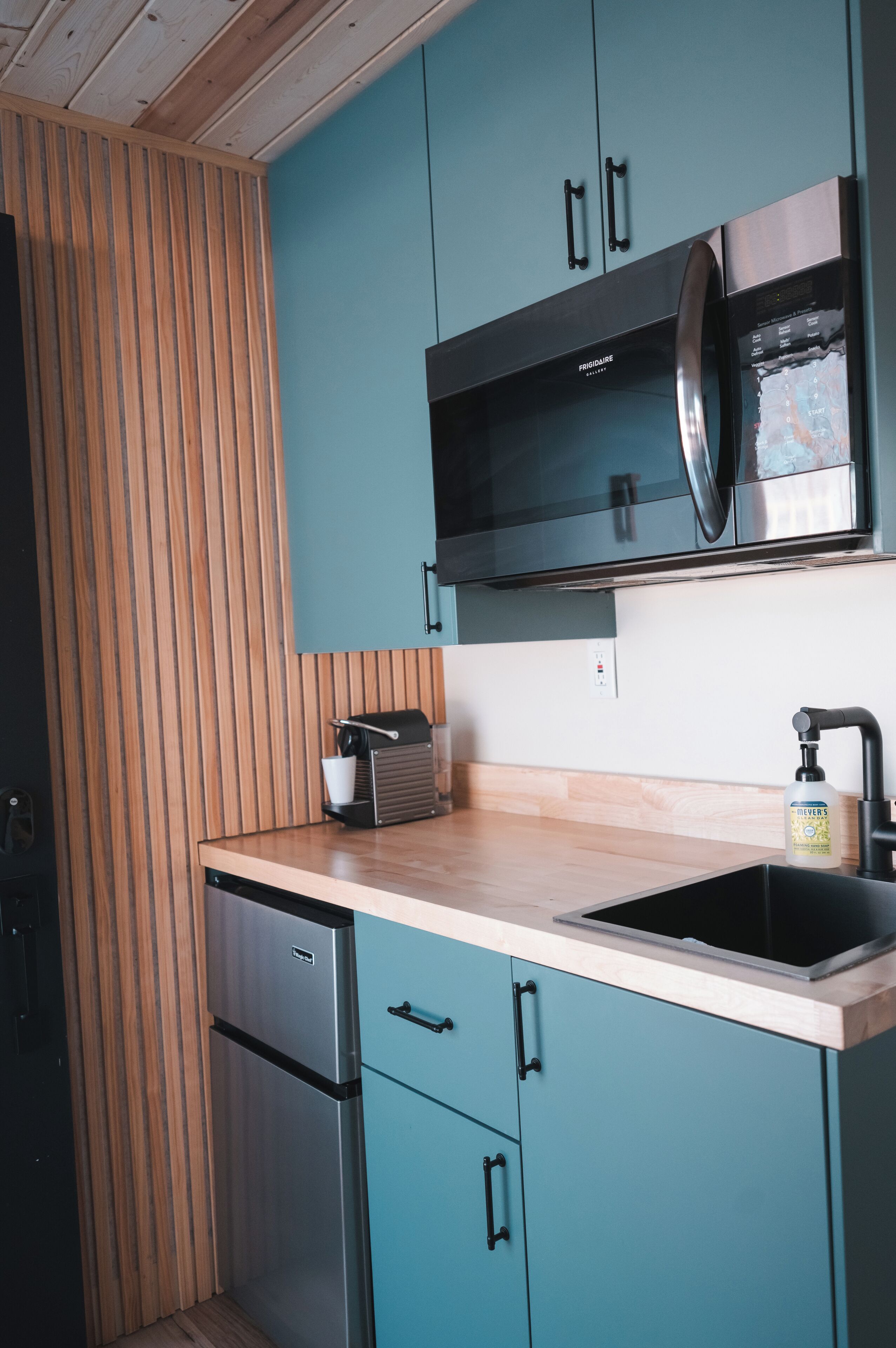 Eine Küche mit türkis-blauen Schränken, einem Edelstahl-Kühlschrank und einer Mikrowelle.