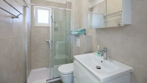Un baño moderno con cabina de ducha de vidrio, inodoro blanco y lavamanos con espejo.