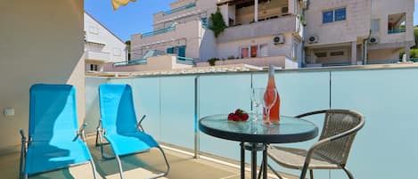 Un balcone con due sedie azzurre, un tavolino rotondo e un bicchiere di bevanda.