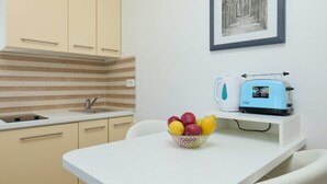 Una cocina con armarios color beige, un salpicadero a rayas, un fregadero, un tostador y un bol de fruta sobre una encimera blanca.